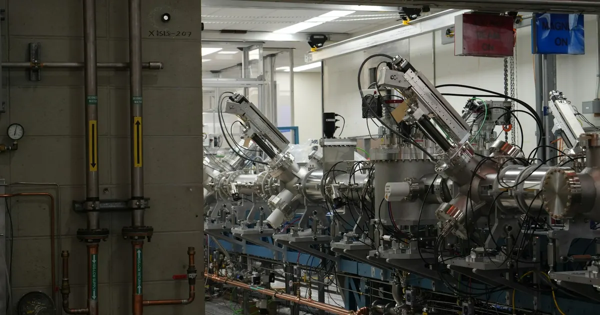 Row of stainless steel vacuum chambers with ports and transfer arms in a research laboratory, the layout behind a load lock chamber