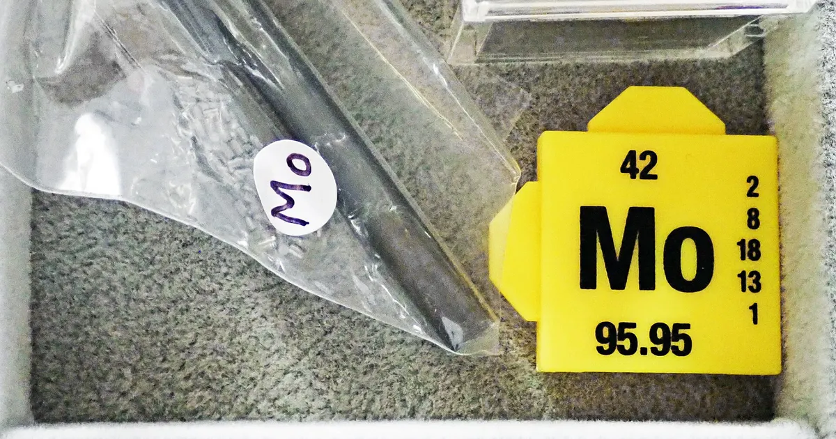 Molybdenum rod in a plastic bag marked Mo beside an element cube, the metal behind molybdenum machining